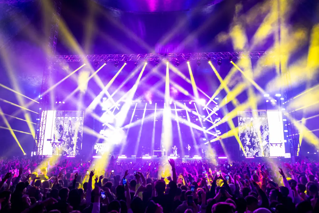 A crowd before a brightly lit performance stage at night